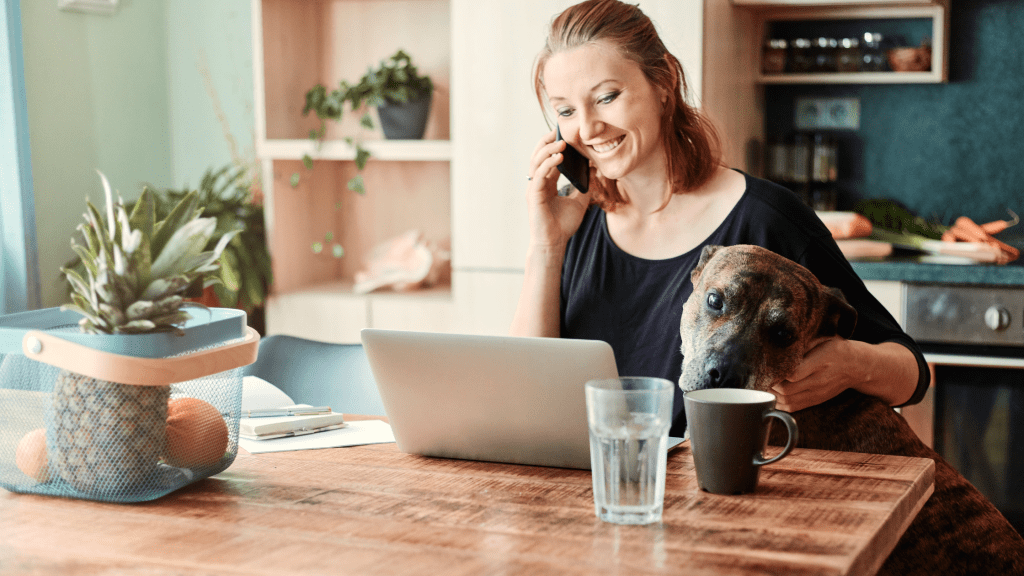 Woman on the phone with her dog and a laptop in front of her